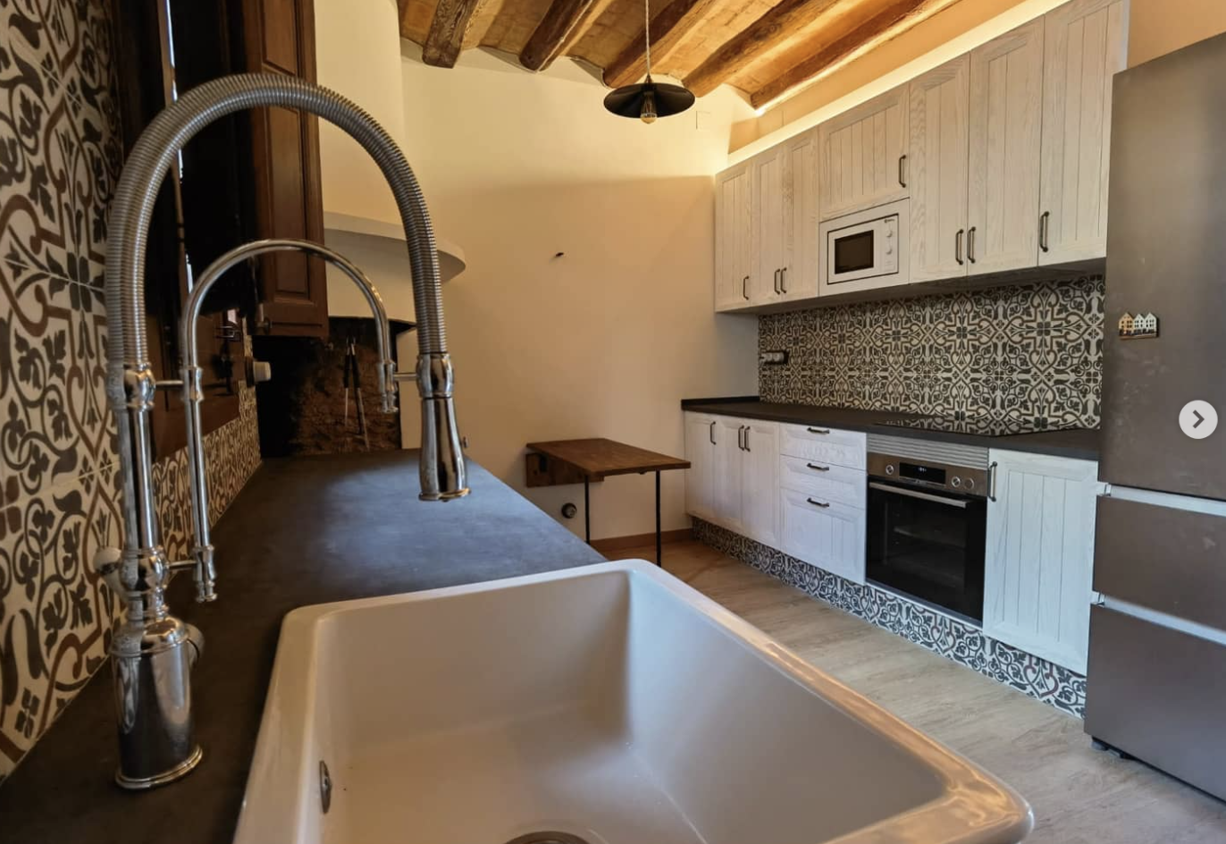 Reforma de cocina rústica con fregadero cerámico blanco, encimera de obra y azulejo decorativo en Masia