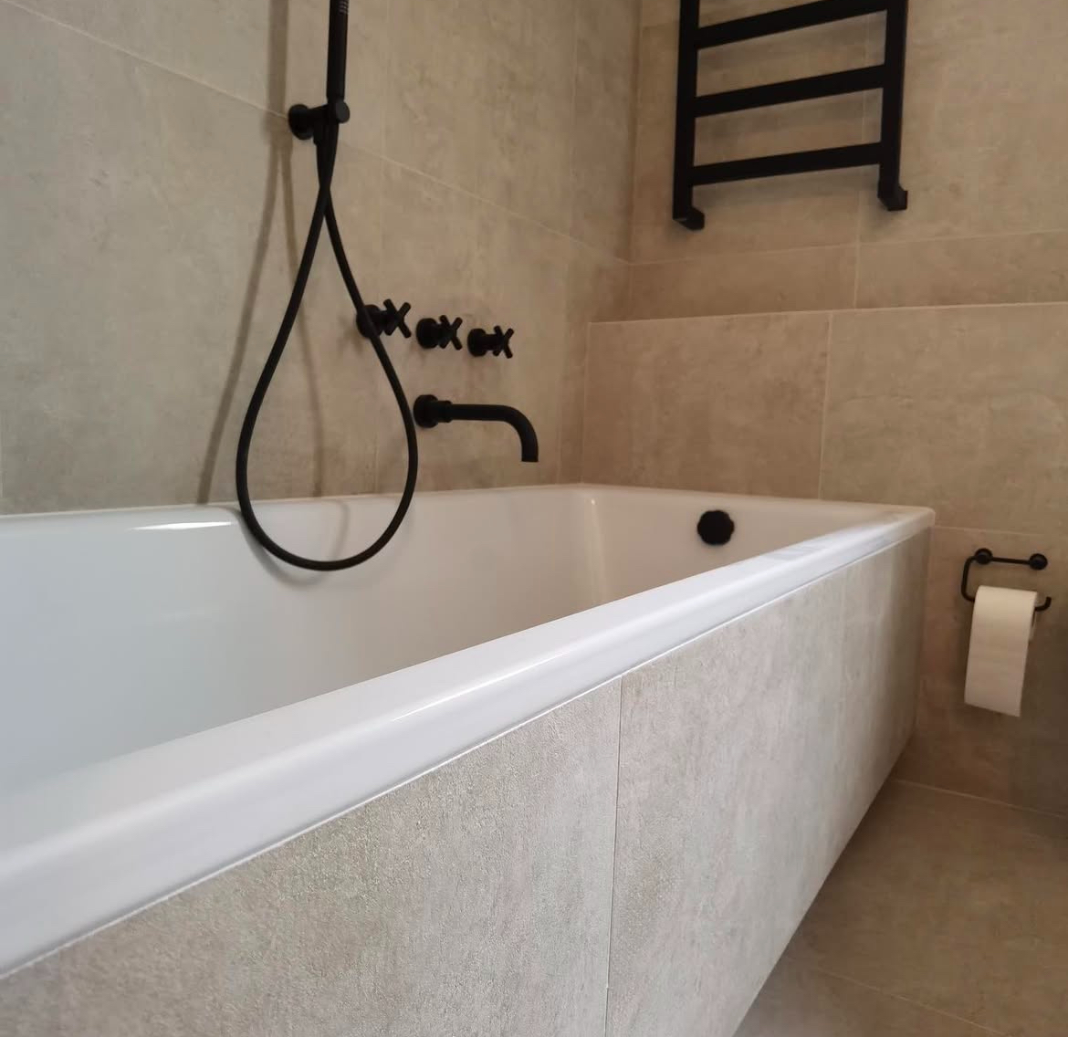 Detalle de bañera integrada con revestimiento porcelánico beige y toallero negro en Eixample Barcelona