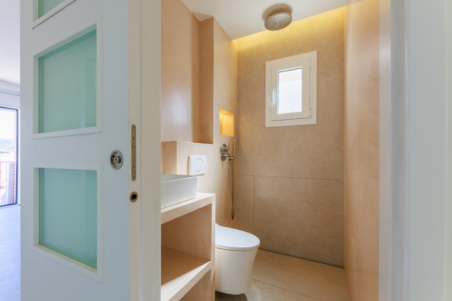 ducha con puerta corredera blanca y vidrio, paredes de micorcemento sahara, ducha alicatada con baldosa en formato grande, mobiliario de obra, hornacinas, luces indirectas